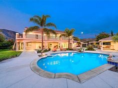 an outdoor swimming pool surrounded by palm trees and landscaping at dusk with the lights on