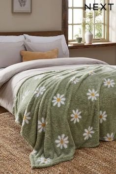 a bed covered in a green blanket with white daisies on it next to a window