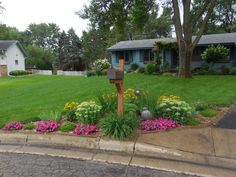 a mailbox sitting in the middle of a flower bed next to a driveway and house