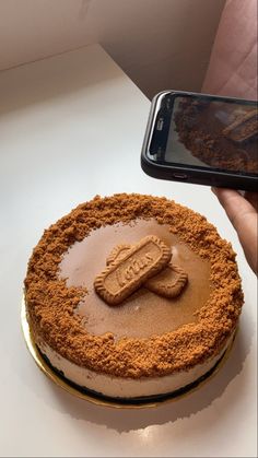 a person holding a cell phone next to a cake on a table with an imprint