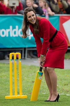 a woman in a red dress playing croquet on the grass with people watching