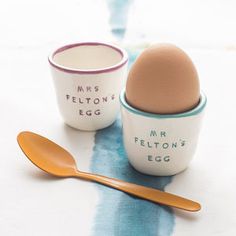 two egg cups with spoons sitting next to each other on a blue and white tablecloth