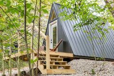 a small cabin in the woods with stairs leading up to it's door and windows