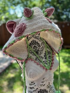 a crocheted hat with pink flowers and green tassels hanging from it's brim