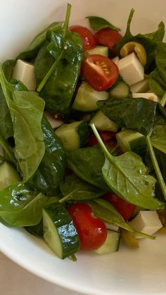 a white bowl filled with spinach, cucumber and tomatoes