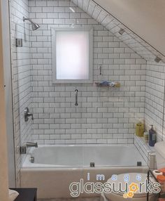 an attic bathroom with white subway tile walls and floor, along with a window above the bathtub