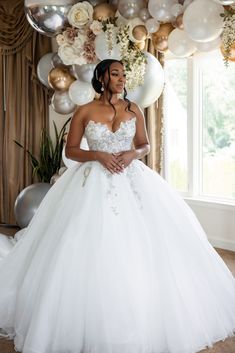 a woman in a white wedding dress standing under balloons and streamers with her hands on her hips