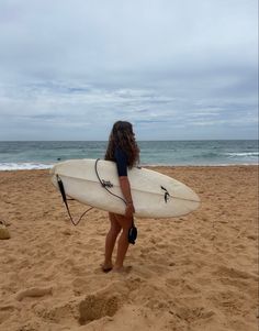 a woman holding a white surfboard on top of a sandy beach