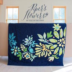 a blue quilt with flowers on it in front of a sign that says piper's flowers by talk of the town