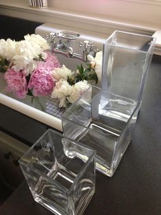 three clear vases sitting on top of a counter next to a sink with flowers in it