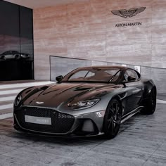 a brown sports car parked in front of a building with the name aston martin on it