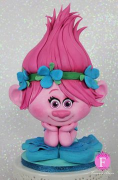 a pink troll with blue flowers on its head sitting on top of a green cake