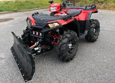 a red four - wheeler parked in a parking lot next to a snow plow