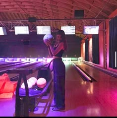 two people standing in front of bowling balls on a wooden floor with purple lights behind them