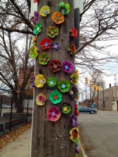 colorful paper flowers are attached to a telephone pole on the side of the road in front of a tree