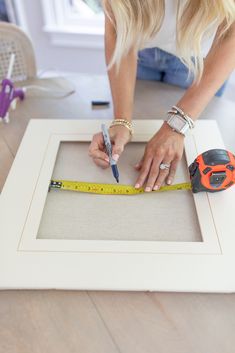 a woman is measuring the width of a frame with a tape measure and a pair of scissors