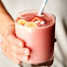 a person holding a glass with a smoothie and strawberries in it on the side