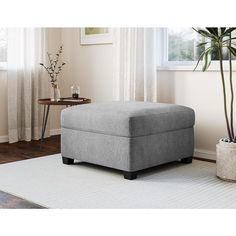 a grey ottoman sitting on top of a white rug next to a plant in a living room