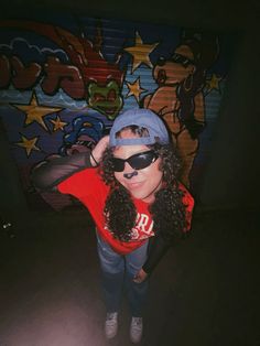 a woman wearing sunglasses and a red shirt is standing in front of a graffiti wall