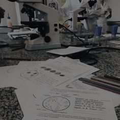 two men in white lab coats working on papers with microscopes and other equipment behind them