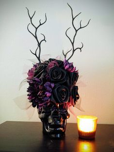 a vase filled with purple flowers next to a lit candle on a wooden table in front of a white wall