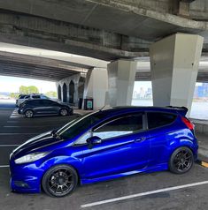 a blue car parked in a parking lot next to an overpass with other cars