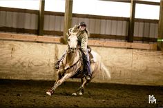 a woman riding on the back of a brown horse in an indoor arena at night