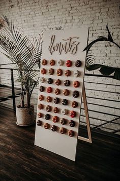 a sign with donuts on it next to a potted plant and brick wall