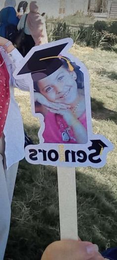 a person holding up a sign with a graduation cap and gown on it's head