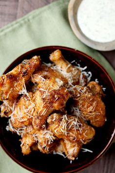 chicken wings with parmesan cheese in a brown bowl on a green napkin next to a cup of yogurt