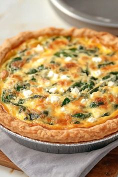 a quiche with spinach, cheese and sauce in a pie pan on a cutting board