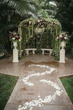 an outdoor ceremony setup with white petals and greenery on the ground, surrounded by palm trees