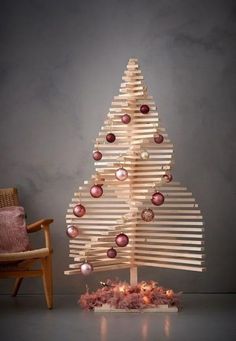 a wooden christmas tree with ornaments and lights on the top, in front of a chair