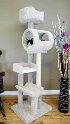 a cat sitting in the corner of a cat tree next to a vase with flowers