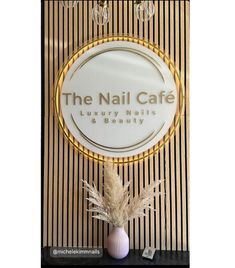 the nail cafe sign is next to a vase with dry grass in front of it