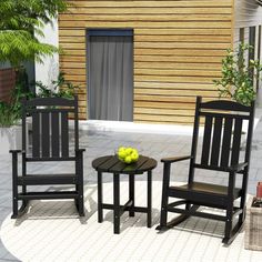 two black rocking chairs and a small table with fruit on it in front of a house