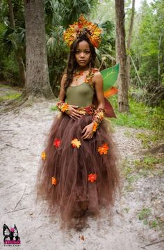 a woman wearing a brown and orange dress with leaves on her head, standing in the woods