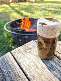 a cup sitting on top of a wooden table next to a fire pit