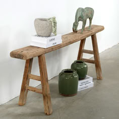 a wooden bench with two green vases on top of it next to a white wall