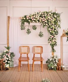 two wooden chairs sitting in front of a floral arch