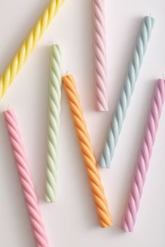 four different colored candles sitting next to each other on a white surface with one candle in the middle