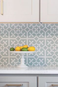 two lemons and three limes in a white bowl on a kitchen countertop