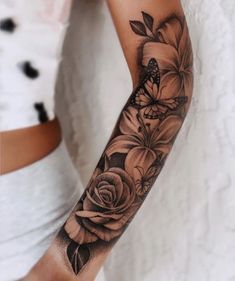 a woman's arm with black and white flowers on the arm, in front of her is a butterfly