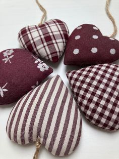 four red and white heart shaped cushions hanging from twine strings on a white surface