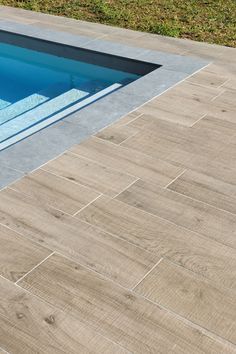 an empty swimming pool in the middle of a grassy area next to a wooden deck