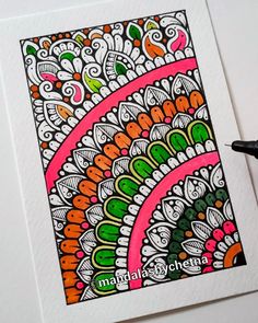 a drawing of a colorful paisley design on white paper next to a black marker pen