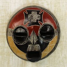 a decorative mask is hanging on the wall in front of a beige background with black and red accents