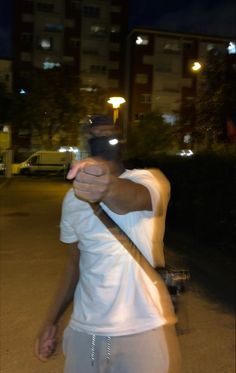 a man in white shirt holding a baseball bat on street at night with buildings in background