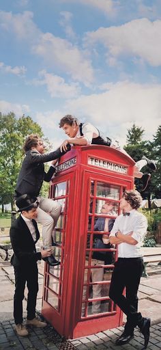 a group of people standing on top of a red phone booth next to each other