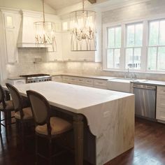 a large kitchen with an island in the middle and white cabinets on both sides, along with marble counter tops